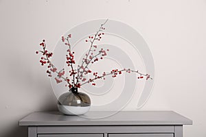 Hawthorn branches with red berries in vase on grey table indoors, space for text