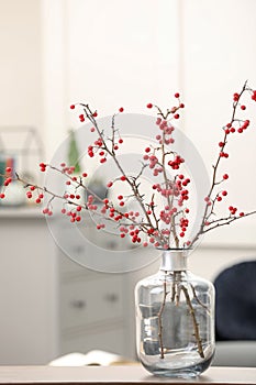 Hawthorn branches with red berries in vase on table indoors