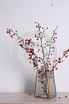 Hawthorn branches with red berries in vase on wooden table indoors