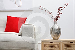 Hawthorn branches with red berries on wooden commode in living room