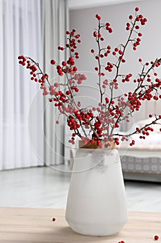 Hawthorn branches with red berries on wooden table in bedroom