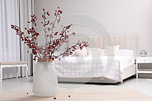 Hawthorn branches with red berries on wooden table in bedroom, space for text