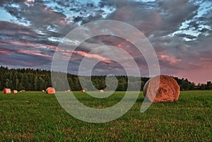 Hay bales on a meadow against beautiful sky with clouds in sunset