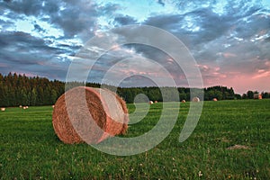 Hay bales on a meadow against beautiful sky with clouds in sunset