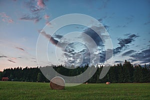 Hay bales on a meadow against beautiful sky with clouds in sunset