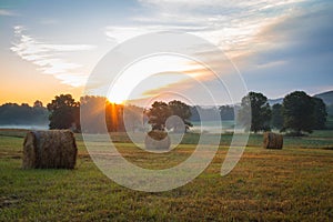 Hay bales rolled on field at sunrise with fog creates amazing sky in early summer