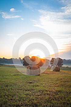 Hay bales rolled on field at sunrise with fog creates amazing sky in early summer