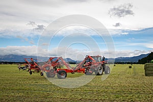 Hay rake attached to a red tractor works on a farm making hay