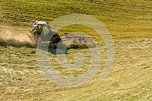 Haymaking on a hillside with rows of hay, a hay tedder and a hay-loader