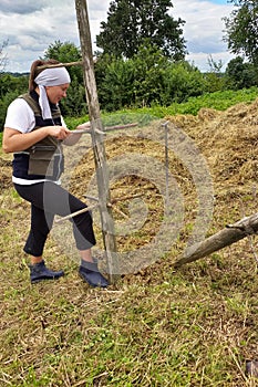 Haymaking season, two village women work in the field, preparing a wooden support for drying hay on it by driving it into the