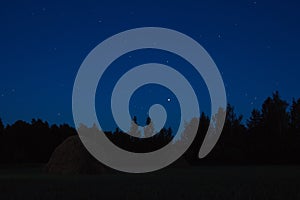 Haystack at night on a field near a forest