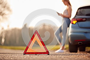 Hazard Warning Triangle Sign For Car Breakdown On Road With Woman Calling For Help In Background