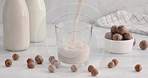 Hazelnut milk. pouring vegan milk into a glass on white table, bottles with non-dairy drinks, white kitchen background