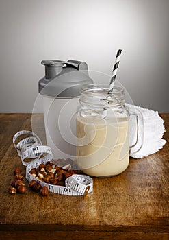 Hazelnut milkshake, ingredients, tape measure and shaker with paper straw on a wooden bench top