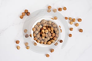 Hazelnut in a white bowl and are scattered on a marble table