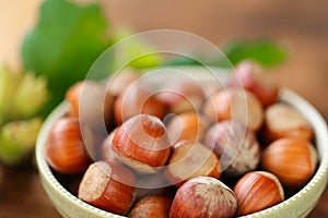 Hazelnuts in a round green bowl with green leaves close-up on a wooden table. Farmed ripe hazelnuts. Nut abundance