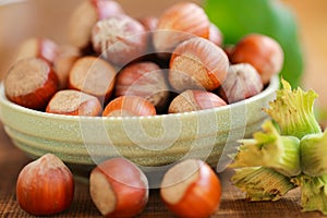 Hazelnuts in a round green bowl with green leaves close-up on a wooden table. Farmed ripe hazelnuts. Nut abundance