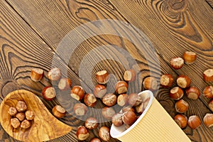 Hazelnuts on a wooden board. Nuts in a disposable eco-friendly glass and olive bowl, flat lay, copy spase