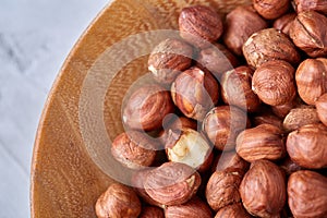 Hazelnuts in wooden bowl on wihite background with copy space, top view, selective focus.