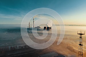 A hazy sunrise silhouettes a factorys smokestack against a polluted sky.