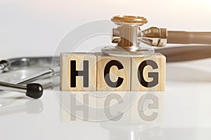 HCG the word on wooden cubes, cubes stand on a reflective white surface, on cubes - a stethoscope