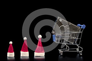 HDD in a shopping basket and three Santa Claus caps in line. Black background. Christmas sale and family discount concept, black