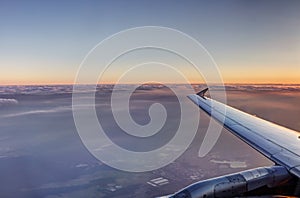 HDR Aerial photo of the landscape under a cloud cover and view stretching all the way to the horizon with an airplane at sunset