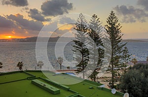 HDR image of a sunset on the horizon behind three trees and a sea