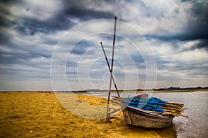 HDR landscape of a boar tied at the corner of river bed sandy beach and cloudy sky day time scene.