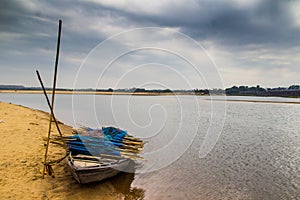 HDR landscape of a boar tied at the corner of river bed sandy beach and cloudy sky day time scene.