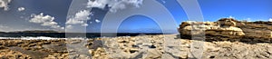 HDR panorama photo of a sunny day at the sea coast with deep blue clean water and a nice stone beach and a large rock on the right