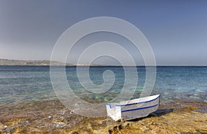 HDR photo of a sunny day at the sea coast with deep blue clean water and a nice stone beach and a small white boat in front