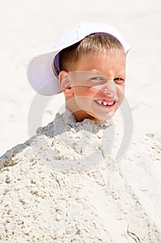 Head of a boy in cap buried in the sand