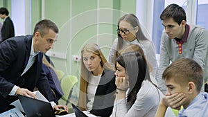 Head of business games help one of the teams. He explains to them using the computer base training game. Young