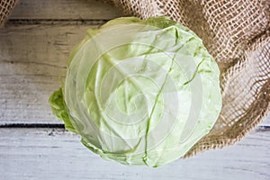 Head of cabbage on sackcloth on white wooden table, top view