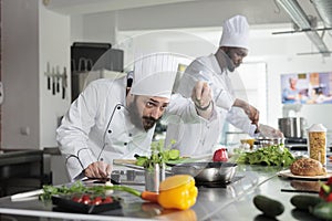 Head chef adding fresh chopped green herbs to food while cooking gourmet dish in restaurant professional kitchen.