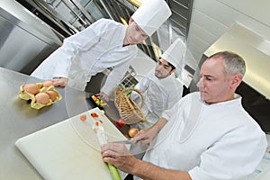 head-chef and apprentices preparing dish in kitchen