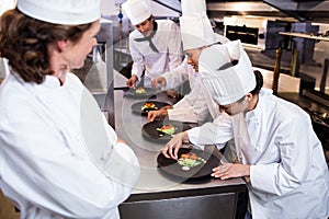 Head chef overlooking other chef decorating dish