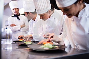 Head chef overlooking other chef preparing dish