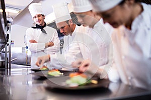 Head chef overlooking other chef preparing dish