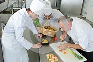 head-chef teaching colleagues how to slice vegetables in kitchen photo