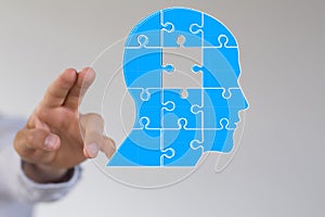 Head consisting of blue pieces of a jigsaw puzzle next to a person's fingers