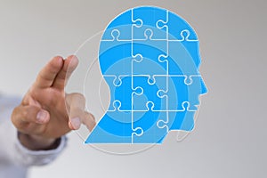 Head consisting of blue pieces of a jigsaw puzzle next to a person's fingers
