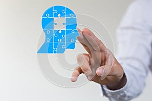 Head consisting of blue pieces of a jigsaw puzzle next to a person's fingers