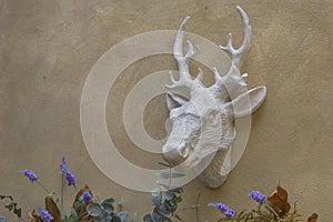 The head of a deer with horns hangs on a textured stucco wall. Garden figurine, decorative decoration.