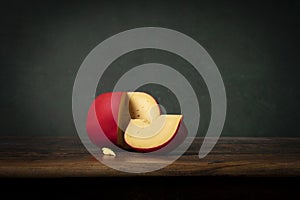 A head of Edam cheese with a red crust lying on a brouwn wooden table with a green background. Rembrandt lightning style photo
