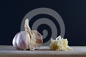 A head of garlic and a pressed garlic releasing allicin against black background