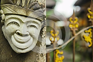 Head of a Hindu deity stone statue of a person with a smile on the background of a fence.