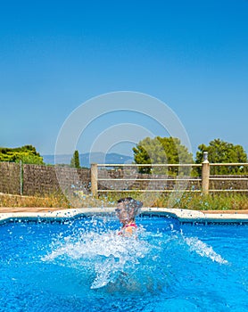 Head of a laughing young woman wearing sunglasses out of the water after jumping from the edge of a swimming pool amidst strong