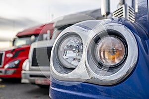 Head light of big rig semi truck with chrome cover standing in row with another semi trucks
